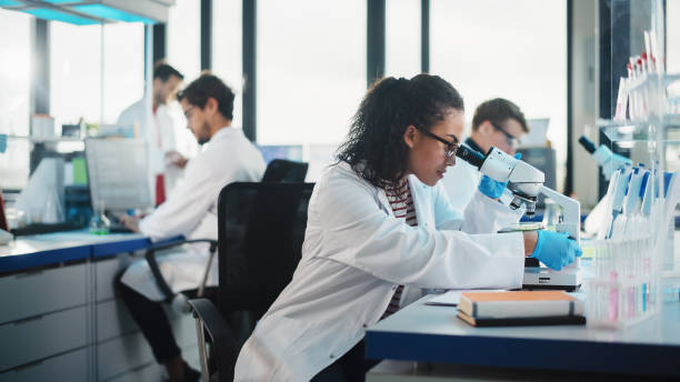istock Medical Science Laboratory: Beautiful Black Scientist Looking Under Microscope Does Analysis of Test Sample. Diverse Team of Young Specialists, Using Advanced Technology Equipment. 1346675535
