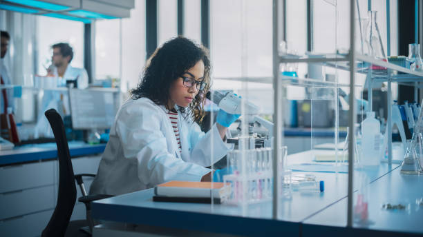 laboratoire des sciences médicales: portrait d’un beau scientifique noir utilise un microscope analyse un échantillon de test. jeune spécialiste ambitieux en biotechnologie, travaillant avec de l’équipement de pointe - scientist research group of people analyzing photos et images de collection