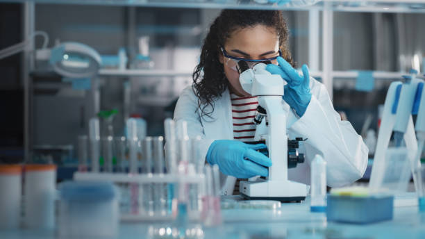 istock Medical Science Laboratory: Portrait of Beautiful Black Scientist Looking Under Microscope Does Analysis of Test Sample. Ambitious Young Biotechnology Specialist, working with Advanced Equipment 1346675586