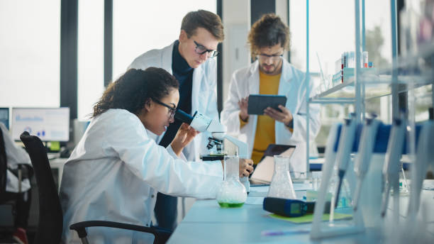 istock Medical Science Laboratory: Shot of Diverse Team Young Scientists Doing Analysis of Test Sample with Use of Microscope. Ambitious Young Biotechnology Specialists, working with Advanced Equipment 1346675607