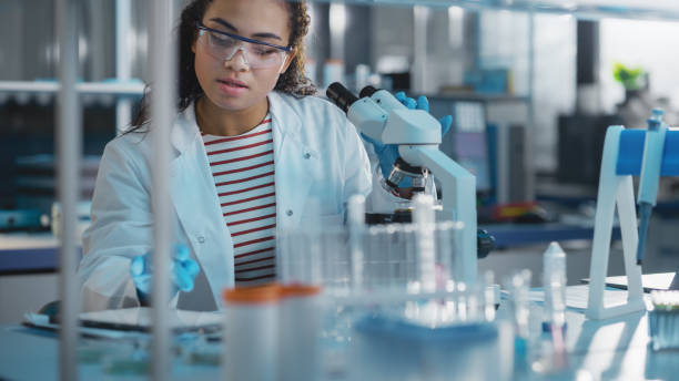 istock Medical Science Laboratory: Portrait of Beautiful Black Scientist Using Microscope, Doing Analysis of Test Sample. Ambitious Young Biotechnology Specialist, working with Advanced Equipment 1346675609