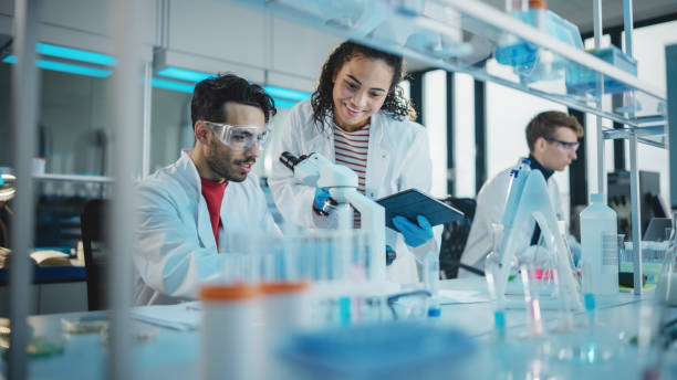 Modern Medical Research Laboratory: Portrait of Latin and Black Young Scientists Using Microscope, Digital Tablet, Doing Sample Analysis, Talking. Diverse Team of Specialists work in Advanced Lab Modern Medical Research Laboratory: Portrait of Latin and Black Young Scientists Using Microscope, Digital Tablet, Doing Sample Analysis, Talking. Diverse Team of Specialists work in Advanced Lab microbiology stock pictures, royalty-free photos & images