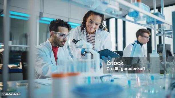 Modern Medical Research Laboratory Portrait Of Latin And Black Young Scientists Using Microscope Digital Tablet Doing Sample Analysis Talking Diverse Team Of Specialists Work In Advanced Lab Stock Photo - Download Image Now