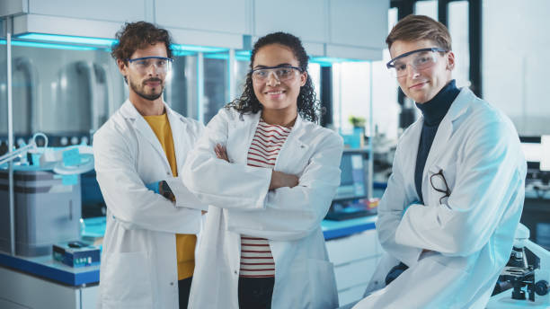 istock Medical Science Laboratory with Team of Three Young Successful Scientists. Beautiful Black Female, Handsome Latin and Caucasian Male Scientists Smile while Looking at Camera. Medium Portrait Shot 1346675648