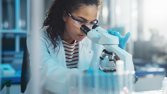 Medical science, woman and microscope in a laboratory for research, analytics and to study particle. Scientist person with glasses for dna or bacteria in lab for innovation, future and biotechnology