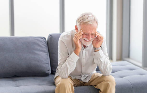 senior man having headache and touching his head while suffering from a migraine in the living room, mature man presses a hand to head suffers from unbearable pain - stressad äldre man bildbanksfoton och bilder