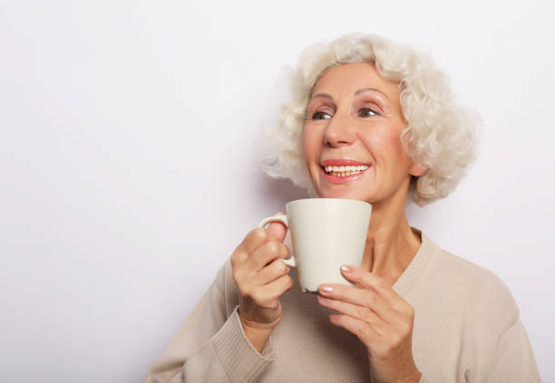istock old excited lady smiling laughing, holding cup drinking coffee, tea, over white background 1346680070