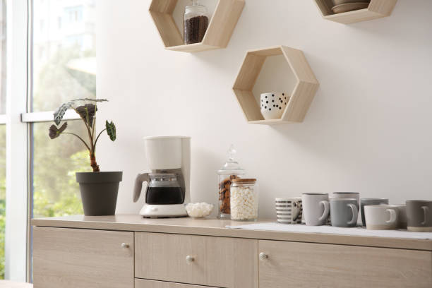 istock Modern coffeemaker and cups on commode near light wall indoors 1346682259