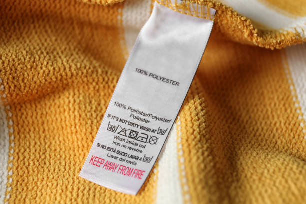 Clothing label with care symbols and material content on yellow shirt, closeup view Clothing label with care symbols and material content on yellow shirt, closeup view polyester stock pictures, royalty-free photos & images