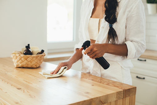 Mujer joven limpiando mesa de madera con spray y trapo natural en una cocina. photo