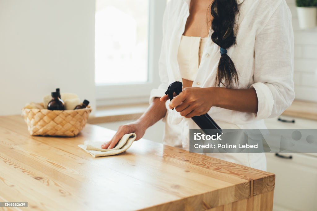 Young woman cleaning wooden table using spray and natural rag in a kitchen. Young woman cleaning wooden table using spray in glass bottle and natural rag in a kitchen. Cleaning Stock Photo