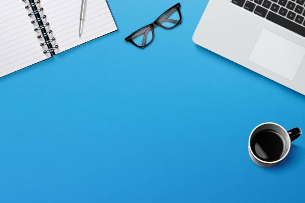 istock Modern workplace with laptop, coffee and notepad on blue background 1346682986