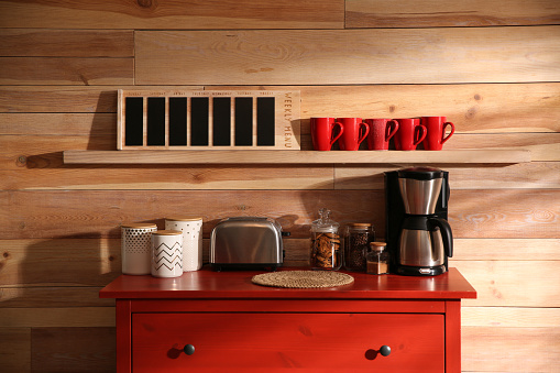 Stylish room interior with modern coffeemaker and toaster on red chest of drawers