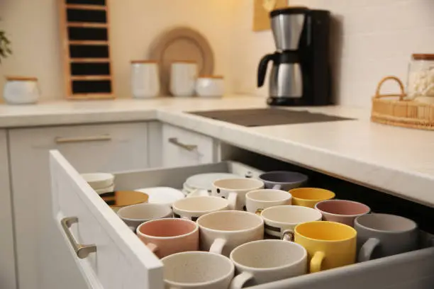 Open drawer with cups and coffeemaker on countertop in kitchen