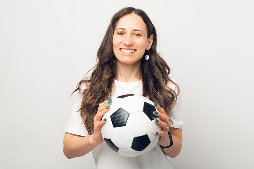 Wide smiling woman is holding a soccer ball and looking at the camera. Portrait over white background.