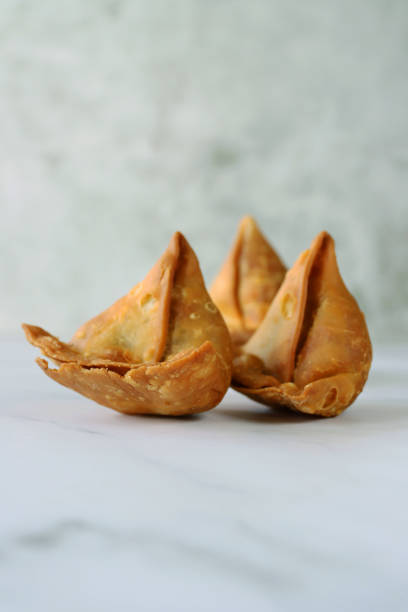 istock Image of three fried samosas, stuffed with spiced potato, peas and meat on a marble effect background, focus on foreground 1346687192