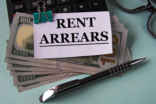 RENT ARREARS - words on a white piece of paper fixed on banknotes against the background of a calculator, glasses and pen. Business and finance concept