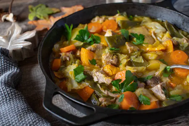 Autumn stew with fresh vegetables, hokkaido pumpkin, potatoes and beans. Cooked with pork ribs and served in a rustic cast iron skillet on wooden table. Sustainable and zero wast dish