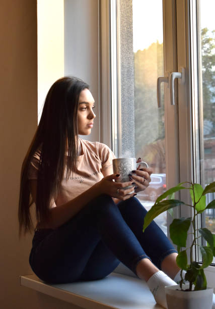 istock the girl sits on the windowsill and drinks coffee 1346690324