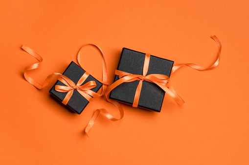 Black gift boxes tied with orange ribbons on an orange background. Halloween concept