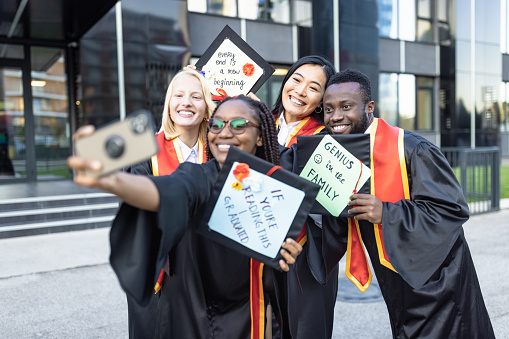 Graduation. Students after graduation ceremony holding their mortarboard with creative messages and taking selfie