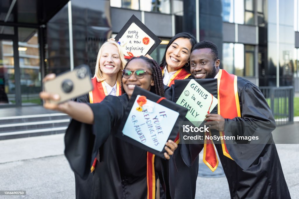 Students after graduation ceremony taking selfie Graduation. Students after graduation ceremony holding their mortarboard with creative messages and taking selfie Mortarboard Stock Photo