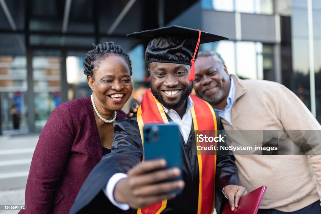 Excited African American college graduate  with his family after the graduation ceremony Excited African American college graduate  with his family after the graduation ceremony taking selfie Graduation Stock Photo