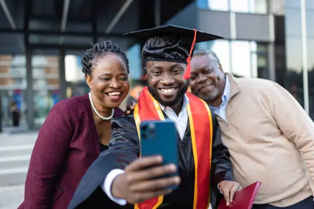 Excited African American college graduate  with his family after the graduation ceremony taking selfie