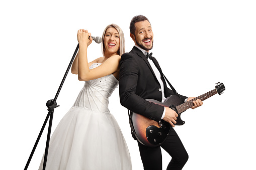 Cheerful bride and groom with a guitar and a microphone singing and smiling isolated on white background