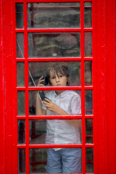 süßer junge, kind, anruft aus einer roten telefonzelle in der stadt - telephone cabin london england telephone booth stock-fotos und bilder