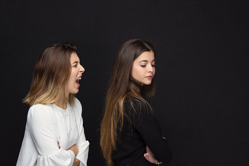 Woman scolding a friend as she turns her back on black background. High quality photo