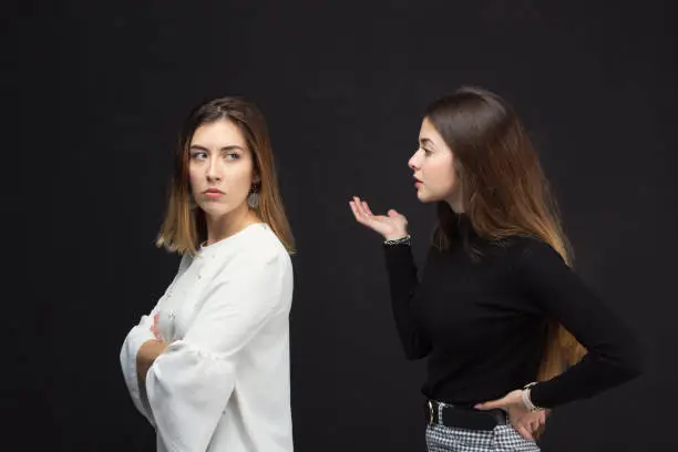 Woman scolding a friend as she turns her back on black background. High quality photo