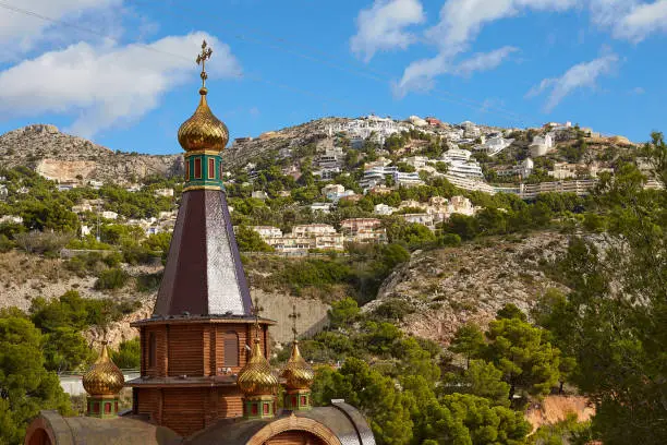 Dome with a cross of the Orthodox Church of St. Michael the Archangel against the background of mountains and blue sky in Altea, Spain