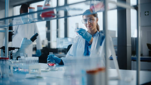 bella scienziata che indossa occhiali protettivi mescolando sostanze chimiche in una provetta in un laboratorio. giovane microbiologa professionista che lavora in un laboratorio moderno con attrezzature tecnologiche. - laboratory test tube student scientist foto e immagini stock