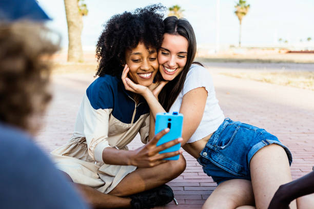Happy multiracial women taking a selfie with smart phone outdoors - Joyful multiethnic female couple having fun with their friends in summer holidays - Millennial generation, friendship and youth concept felices amigas multirraciales tomándose una selfie con un teléfono inteligente al aire libre - alegre pareja femenina multiétnica divirtiéndose con sus amigas en las vacaciones de verano - generación millennial, amistad y concepto juvenil