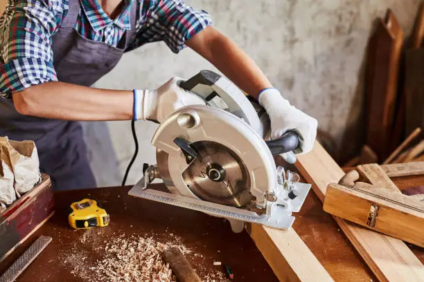 Photo of Skilled female carpenter using a circular saw. Woman worker in the carpenter workroom renovation. Small business concept