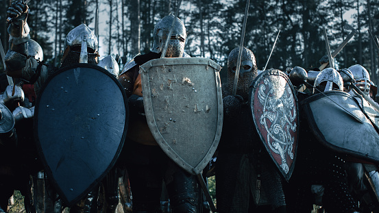 A medieval knight wearing full armour and helmet, holding a flag on a pole, sits on a horse riding on grassy coastal land over rocky hills towards a large distant castle on a rocky outcrop at dawn/dusk as a stormy cloud looms overhead. An eagle leads the way.