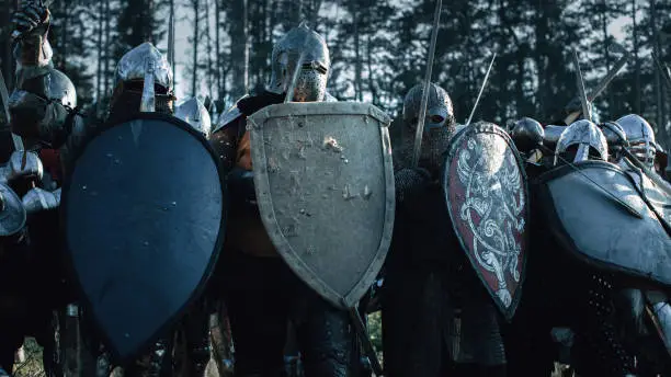 Photo of Epic Invading Army of Medieval Knights on Battlefield, Plate Body Armored Soldiers Hit Shields with Swords in Battle Cry. War and Conquest. Historical Reenactment.