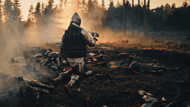 istock Medieval Knight Walking on Battlefield amidst Dead Enemies. Surviving Crusader, Soldier, Warrior after Battle. Smoke and Destruction of War, Invasion, Crusade. Dramatic, Cinematic Historic Reenactment 1346709113