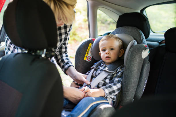 The hands of a woman are fastening the security belt to happy child, who is sitting in safety car seat (chair). stock photo