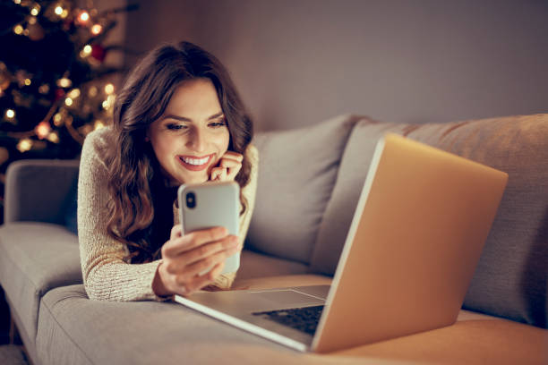 Beautiful young woman paying with mobile phone for online shopping ordering Christmas presents stock photo