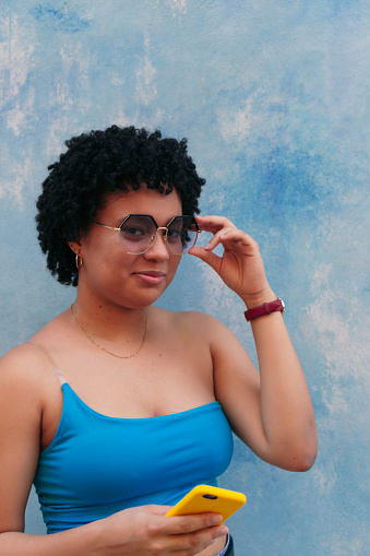 Pretty afro woman wearing a blue blouse laughing in front of a blue background. She is looking at the camera