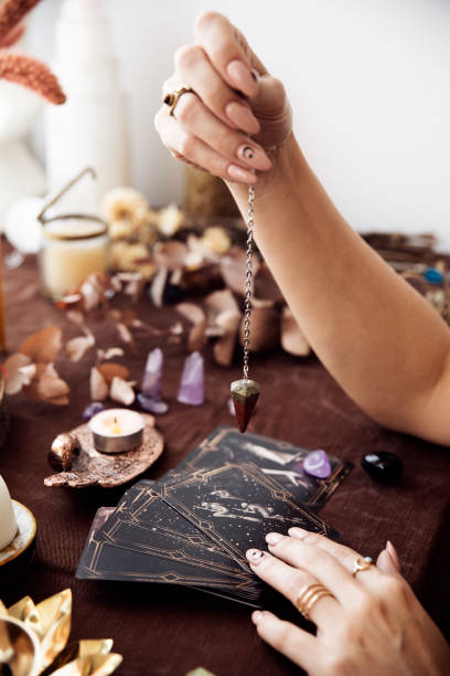 A woman holds a pendulum over the deck of tarot cards A woman holds a pendulum over the deck of tarot cards at her fall colored witch altar crystal altar stock pictures, royalty-free photos & images