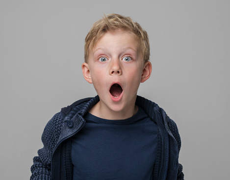 Portrait of surprised boy with mouth open standing against gray background.