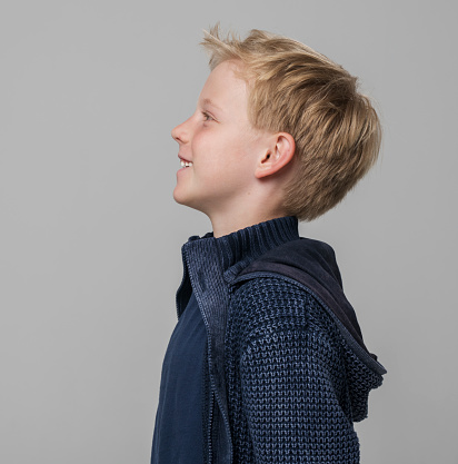 Side view of smiling boy looking up while standing against gray background.