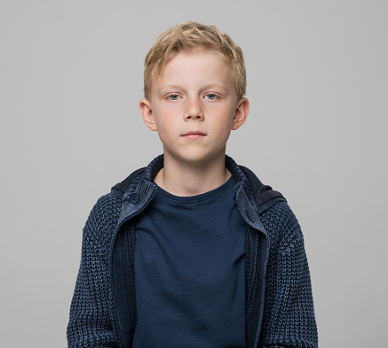 Portrait of boy wearing blue jacket while standing against gray background.