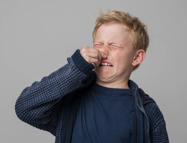 Close-up of boy holding nose Portrait of boy holding nose while standing against gray background. holding nose stock pictures, royalty-free photos & images