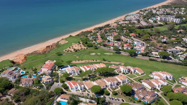 Aerial overview of Quinta do Lago resort buildings in Vale de Lobo, Algarve, Portugal, Europe. Shot of rooftops of luxury cottages in green landscape with mountains on background. Golf fields.