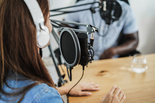 Anfitriones multirraciales haciendo entrevistas mientras transmiten podcasts juntos en el estudio en casa - Concéntrese en el micrófono photo
