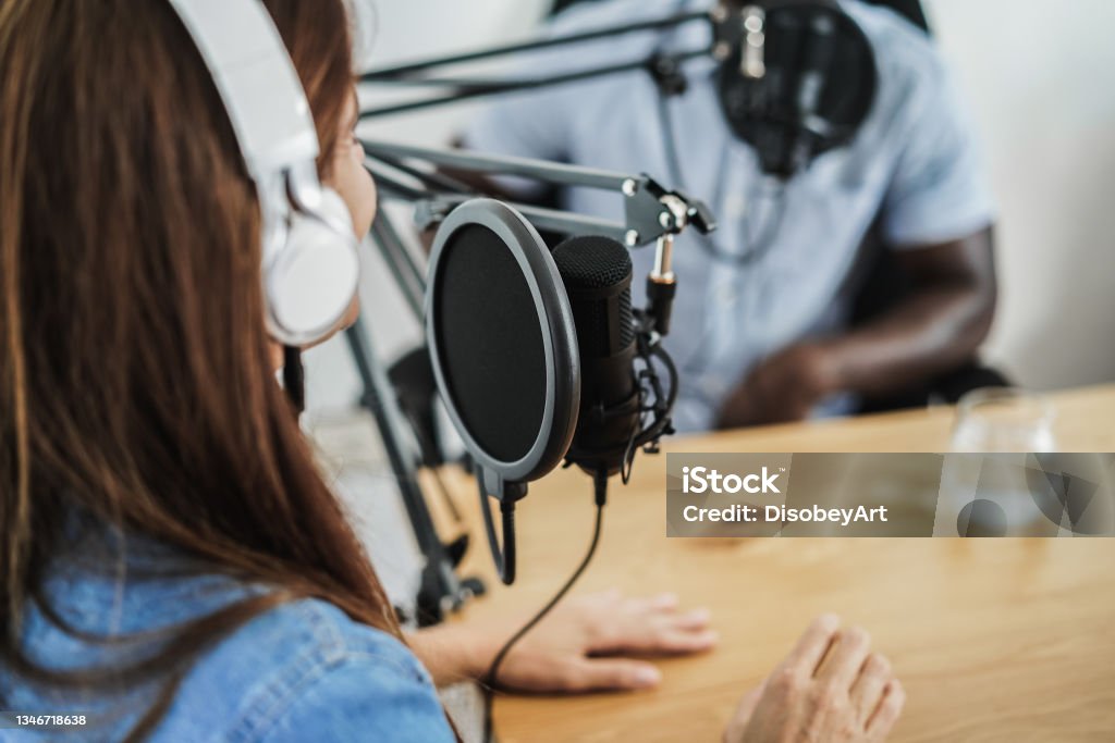 Multiracial hosts doing interview while streaming podcast together at home studio - Focus on microphone Podcasting Stock Photo